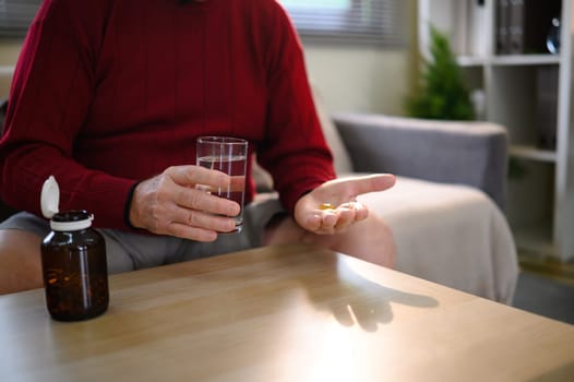 Close up of senior man holding pills and a glass of water near a pill bottle.