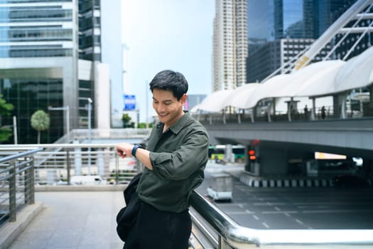 Adult businessman standing on an urban walkway, checking his smartwatch.