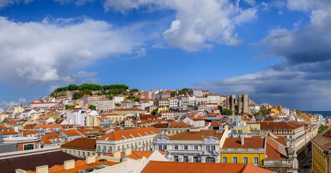 Scenic panoramic view of Lisbon historic Alfama district, St George castle on hill top with lush foliage, Gothic cathedral Se and colorful houses with terracotta rooftops on sunny day, clear blue sky and dramatic clouds. Famous travel destination.