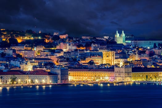 Lisbon historic old town with vibrant city lights under dramatic night sky. Praca do Comercio or Commerce square and iconic landmarks by waterfront of Tagus river, cityscape after dark, churches and cathedrals, scenic view of hilltop castle Sao Jorge