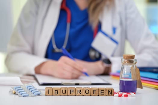 A healthcare professional is writing a prescription for ibuprofen, with medication bottles in plain sight