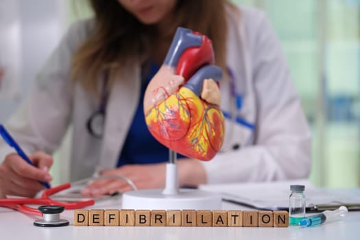 A healthcare professional examines a heart model, focusing intently on the defibrillation procedure