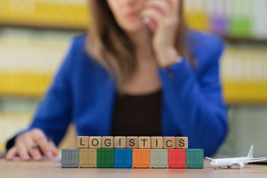 A focused woman in logistics management, showcasing blocks spelling 'LOGISTICS' amid a professional setting.