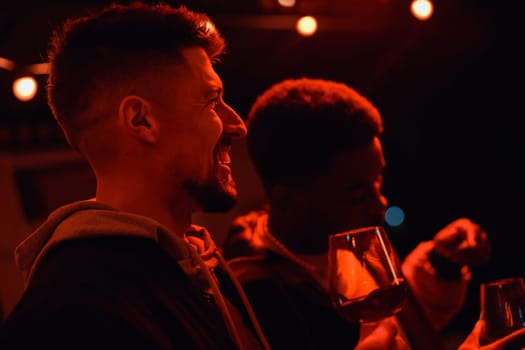 Two friends share laughter and conversation while holding glasses during a cozy evening gathering. Warm lights create a vibrant yet relaxed ambiance.