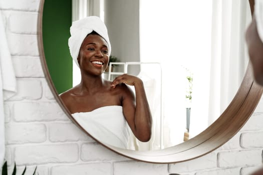 A woman enjoys a moment of self-care in the bathroom, smiling confidently at her reflection in a round mirror. The bright setting adds to her joyful expression.