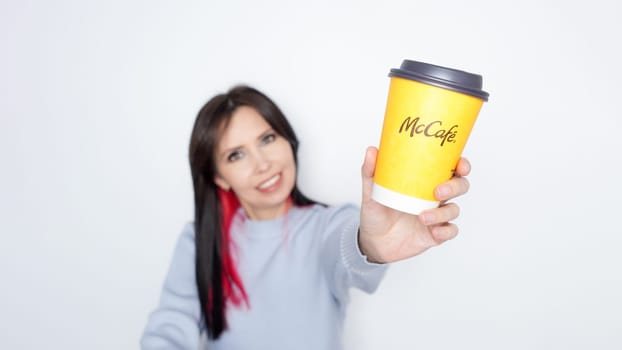 Ottawa ON Canada -2024-10-28: Cheerful woman with long dark hair holding McDonalds yellow coffee cup joyfully on white background.