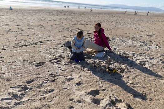 Mother and child enjoying a sunny day, building sandcastles and playing with toys on a beautiful sandy beach