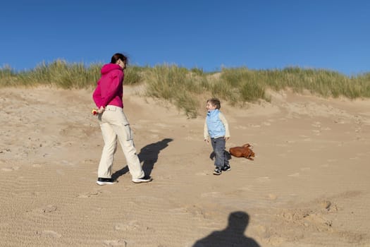 Mother and son enjoying a sunny day playing together on the beach near sand dunes