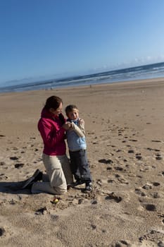 Mother kneeling on the sand and comforting her son on a sunny beach