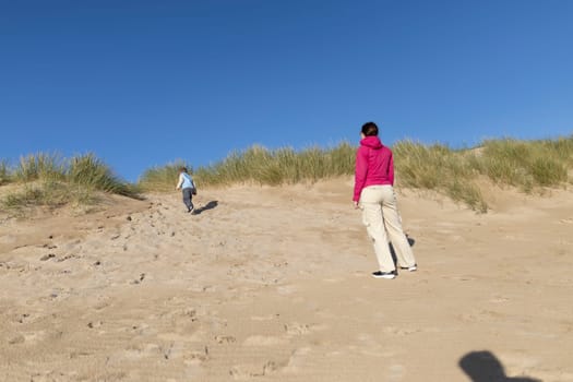 Mother and child enjoying a sunny day at the beach, climbing sand dunes and exploring nature