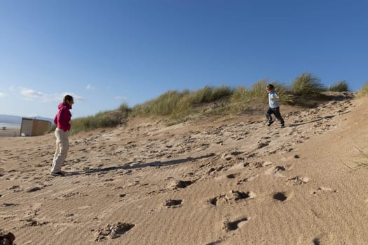 Mother and son enjoying a sunny day at the beach, playing on the sand dunes