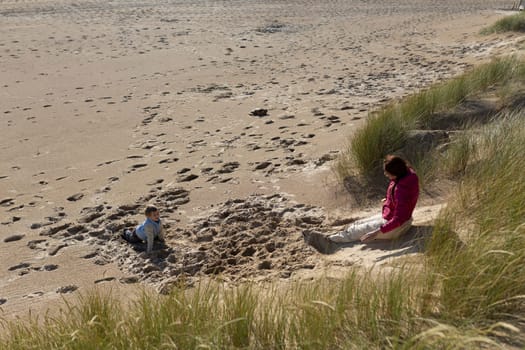 Mother and son enjoying a sunny day, playing on the sand near grassy dunes