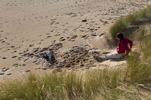 Mother and son enjoying a sunny day at the beach, playing in the sand near the dunes