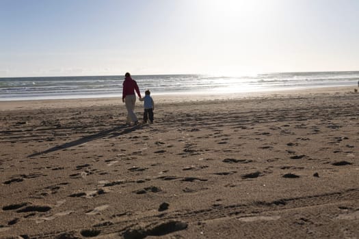 Mother and son enjoying a leisurely stroll along a sandy beach at sunset