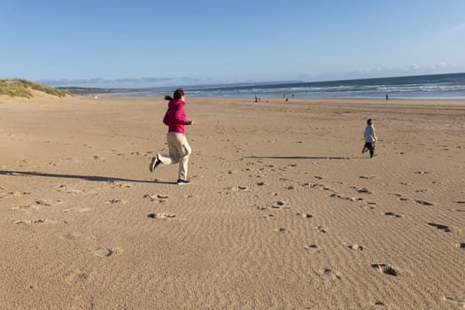 Mother and son running on a deserted beach towards the ocean on a sunny day