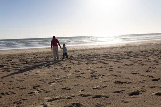 Mother and son holding hands walking on a beach towards the ocean at sunset