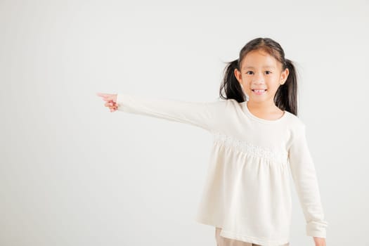 Happy Asian portrait cute young kid girl smiling indicate finger empty space, studio shot isolated on white background, Thai kindergarten child pointing index out with copy space
