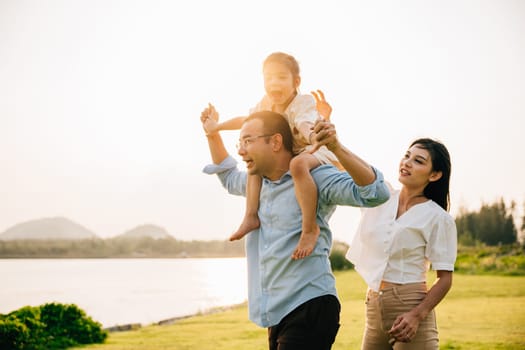 Asian family child girl piggyback riding back on father raising hands like flying outdoor nature park with mother, Happy parent daughter having fun together, Tourist lifestyle family leisure activity