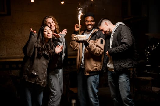 A group of friends enjoys a fun evening celebration outdoors, holding a cake with sparklers. Laughter and happiness fill the air as they share this special moment.