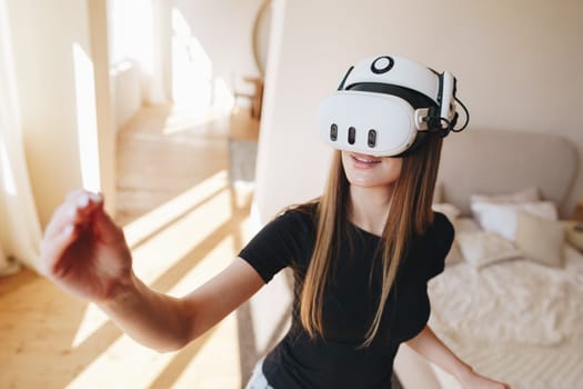 A young woman engages with virtual reality equipment in a contemporary living space. Sunlight streams through large windows, creating an inviting atmosphere.
