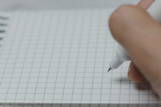 Woman's hand writing on grid notebook with white pen. Concept of studying, planning, journaling, creativity, education, and productivity in a minimal workspace.
