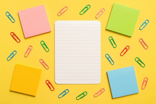 Top view of a notebook sheet with colorful sticky notes and scattered paper clips on a yellow background. Great for school designs, planning visuals, back-to-school themes and organizational content