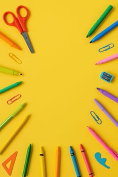 Colorful stationery items like pens, crayons, scissors, and clips arranged in a circular frame on yellow background. Perfect for school visuals, educational ads, or playful learning designs