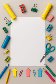 Flat lay of colorful school supplies including pencils, sharpeners, glue sticks and paperclips arranged around a white sheet on grey background. Great for education visuals and design projects