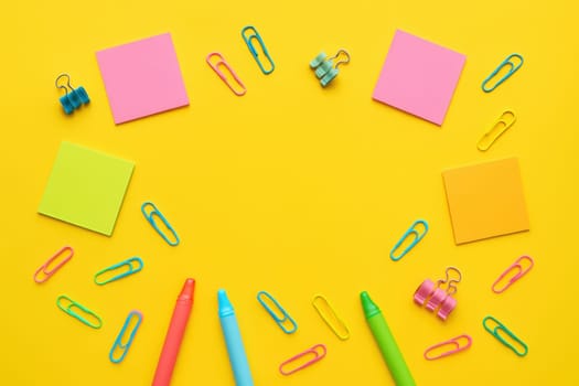 Brightly colored school supplies such as crayons, paper clips, and sticky notes scattered on a yellow background. Ideal for educational themes, creative visuals, and back-to-school designs