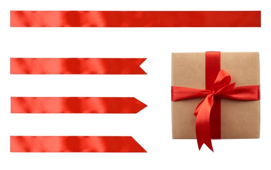 Kraft paper gift box tied with red satin ribbon with bow and set of red ribbons of different shapes on isolated background