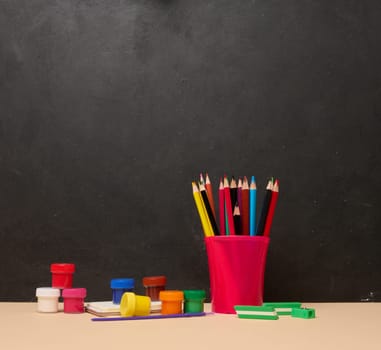 Pink glass with writing utensils, paint cans, brush, creativity or school activities