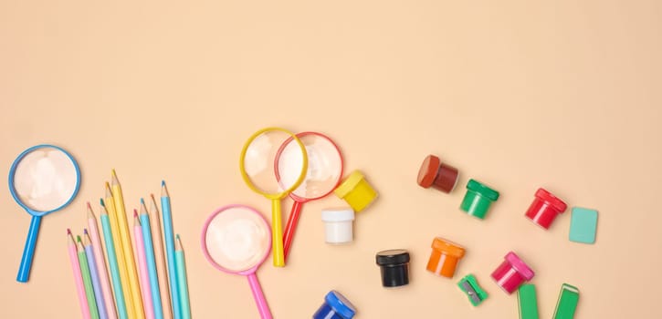 A collection of brightly colored school and office supplies, including pencils, magnifying glasses, paper clips and erasers, scattered on a neutral background