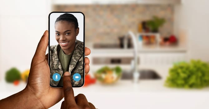 A person interacts with a friend on a video call using a smartphone in a cozy kitchen. Fresh ingredients visible in the background add a touch of warmth and homey atmosphere.