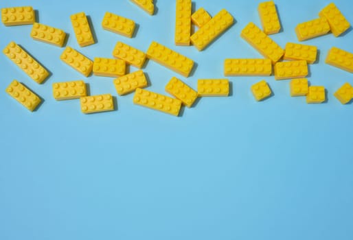 Scattered blue plastic toy building bricks on a solid yellow background. Play, construction, education or creative concept