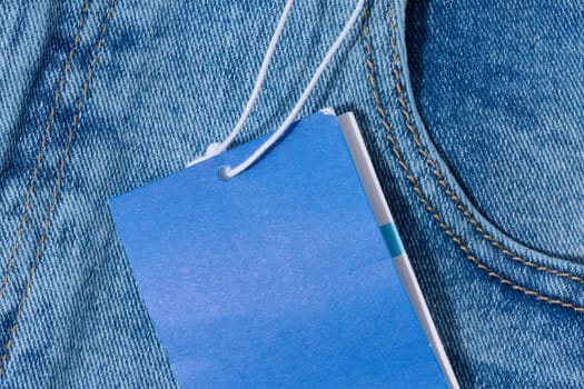 Close-up of light blue denim jeans with a blank blue price tag attached to the belt loop. 