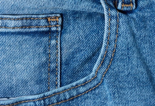 Close up of blue denim jeans showing a front pocket corner with distinct orange stitching detail