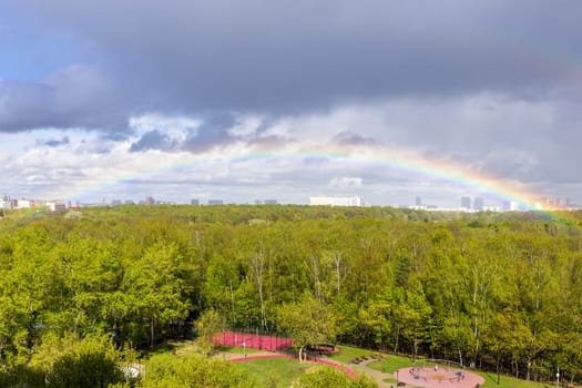rainbow over green city park and playground after rain on sunny spring day