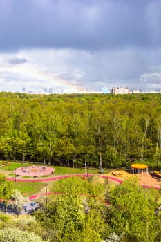 sunlit playground and green city park after rain with rainbow on sunny spring day