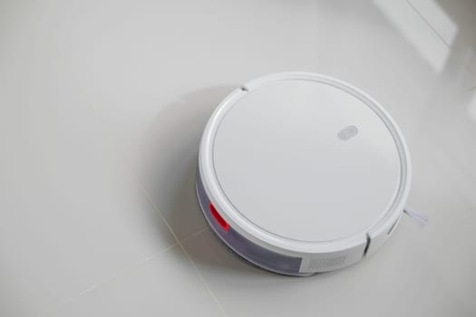White automatic floor cleaner with side brush on tile flooring, designed for efficient cleaning. Robot vacuum concept of smart home technology for seamless, wireless cleaning of various surfaces