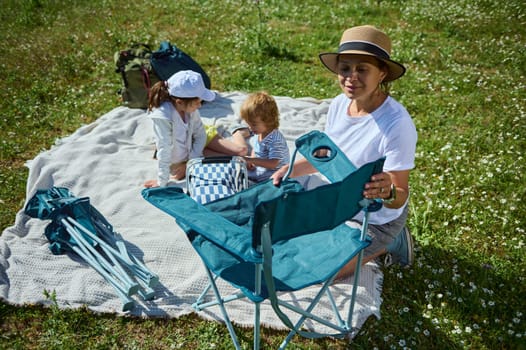 A family gathers for a picnic on a sunny day, enjoying time together in a lush grassy meadow surrounded by flowers. Perfect setting for camaraderie and outdoor relaxation.