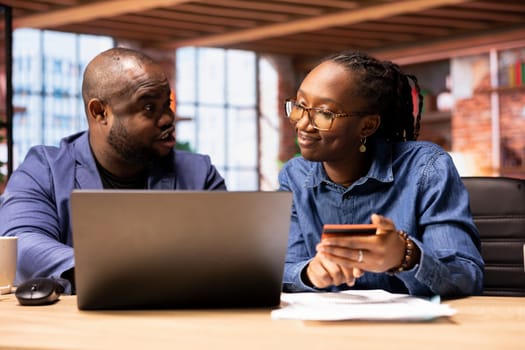 Mature couple managing online banking and payments with the credit card, entering digits on a website to confirm the money transfer. Casual people at home office makes transactions.
