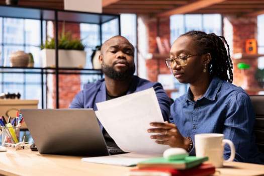 Black man and woman creating a report with information from papers and archived files, improving networking skills and achieving career independence. Remote workers solving tasks.