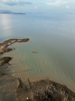 Drone shot of tropical sailboats in a turquoise bay near the harbor, boats floating in crystal clear water near a scenic Thai island with rocky beach. Picturesque shoreline with fun activities.
