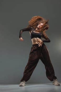 Jazz-funk dancer in fierce motion with flying hair, black outfit, and bold pose on grey studio background.