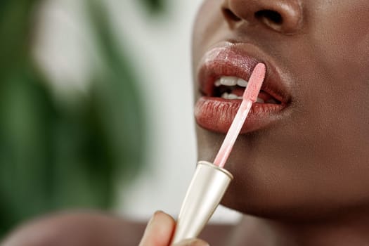 In a well-lit environment, a person applies a soft pink lip gloss to their lips. The focus is on the careful application, highlighting the smooth texture and vibrant color.