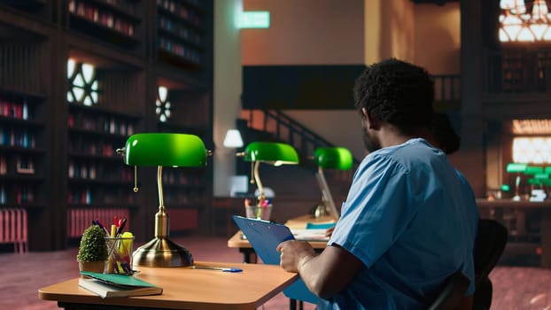 Future nurses studying anatomy class notes in a university library, reviewing courses and preparing for exams. Black med school students working together for their medical education. Camera A.