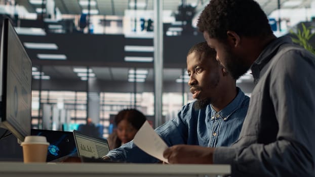 Business manager sits with a worker to review financial forecasts on pc, leading an analytics evaluation on project development. Achieving organizational goals for growth. Camera A.
