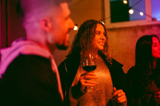 A group of friends is gathered in a warm, colorful outdoor environment, holding drinks and sharing smiles. They are enjoying a lively evening filled with conversation and laughter.