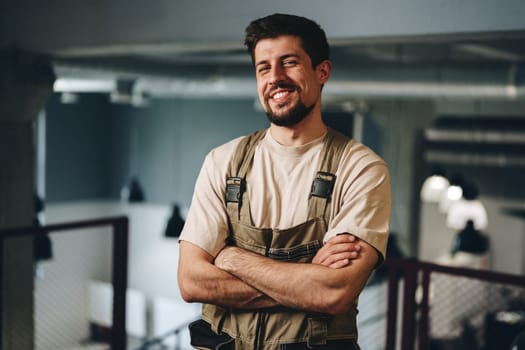 A young man with a hearty smile poses confidently in a contemporary workspace. He wears work attire and exudes a sense of professionalism and approachability.