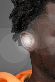 A close view highlights a person's ear and a modern hearing device, accentuated by an orange garment. The gray background adds depth, focusing on technology and individuality.